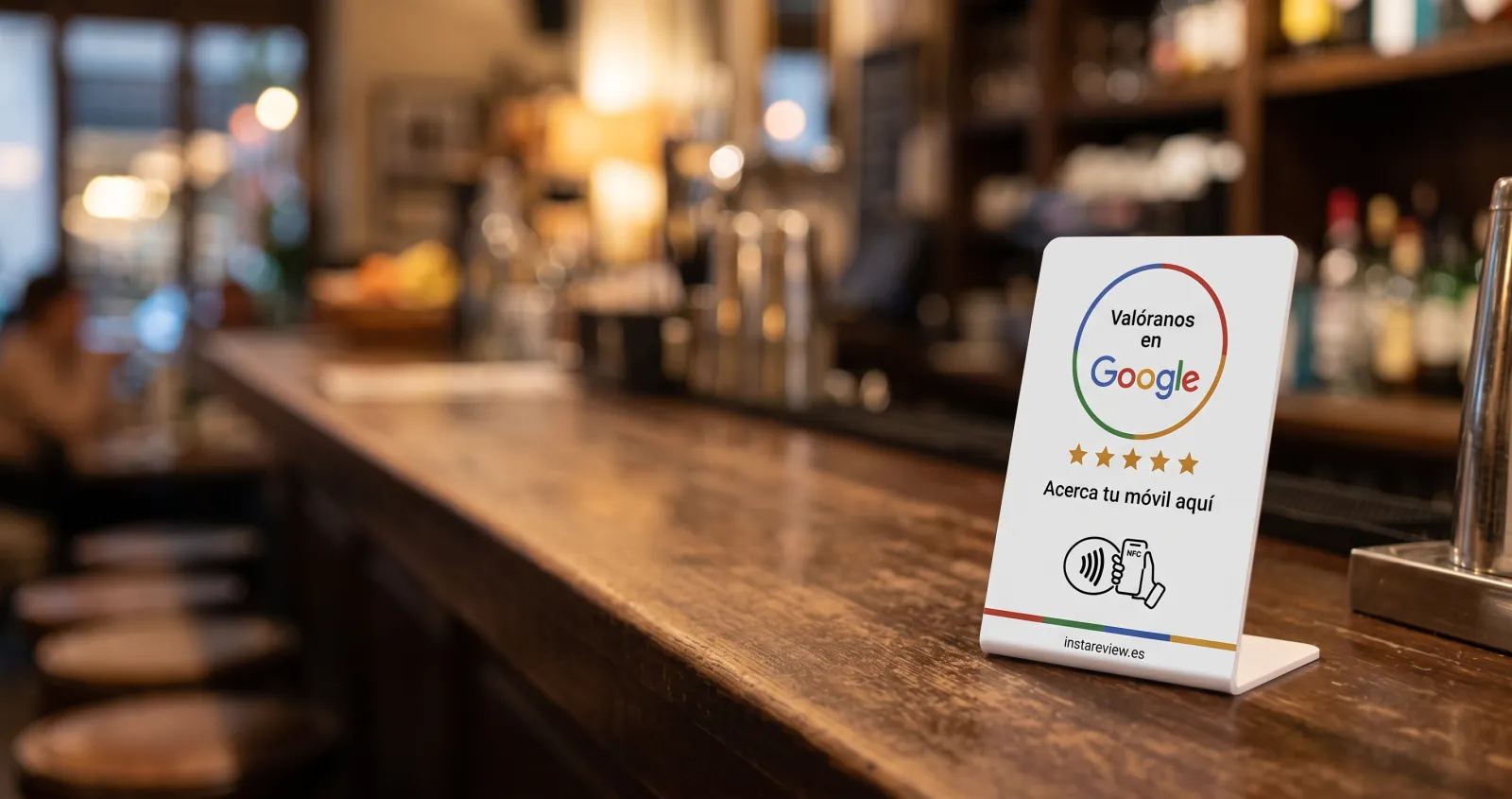 Expositor NFC «Valóranos en Google» de Instareview en la barra de un bar, con botellas y taburetes al fondo